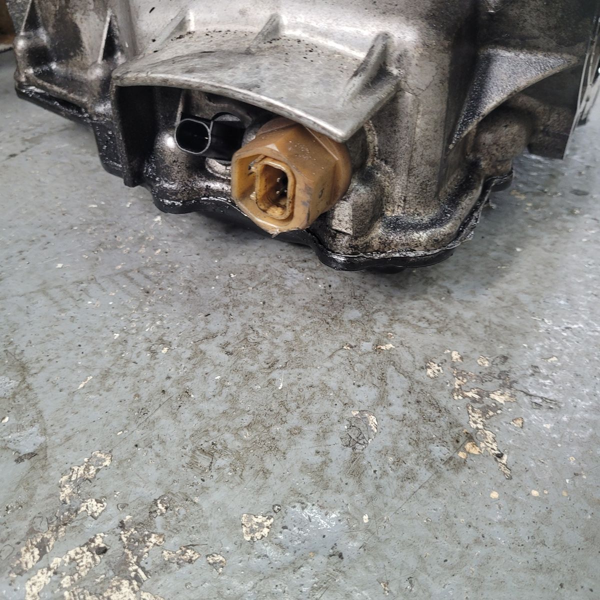 Automotive Oil Temperature Sensor on Engine Block A brown oil temperature sensor attached to a silver engine block on a workshop floor