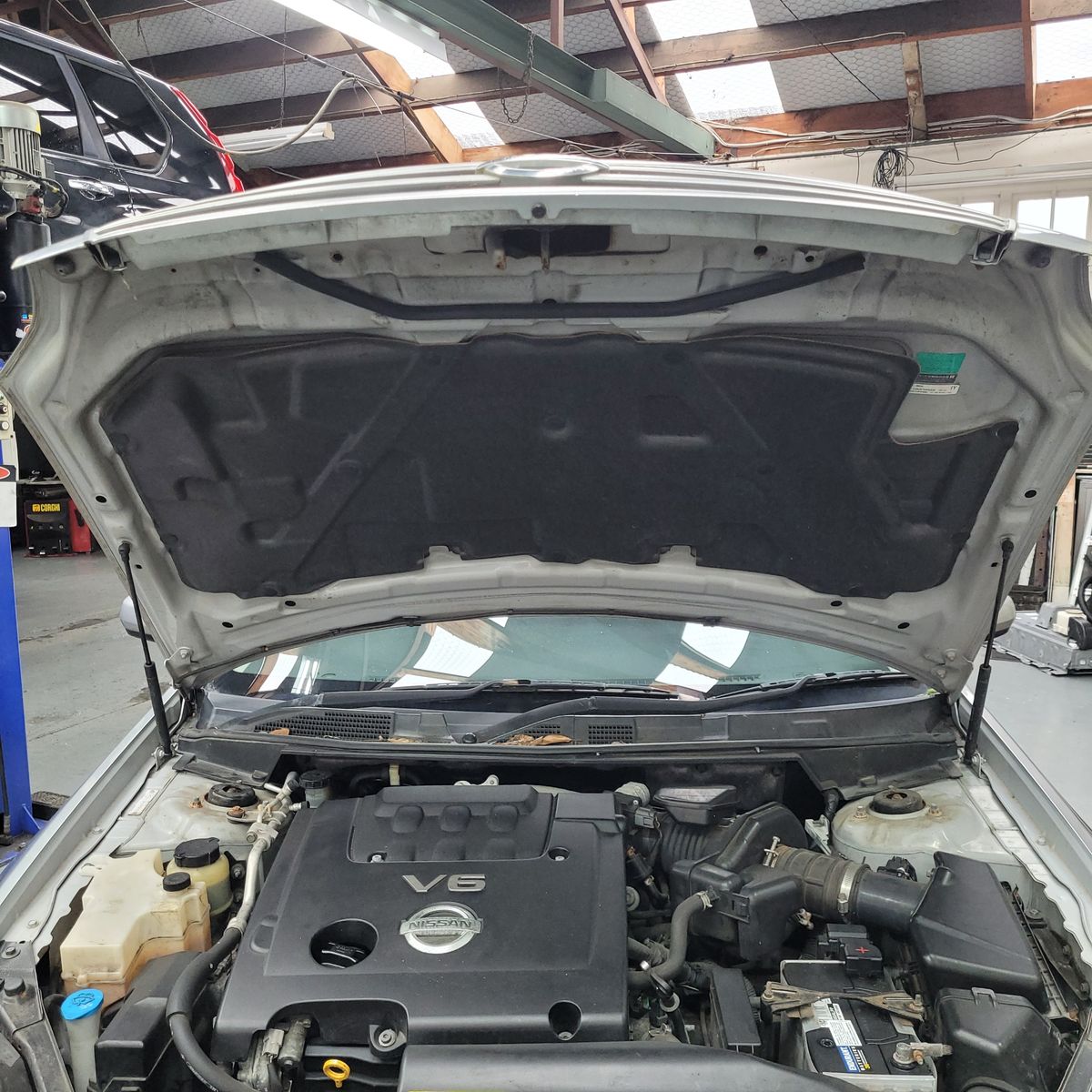 Open Car Bonnet Showing Nissan V6 Engine Nissan V6 engine under an open car bonnet in a garage.