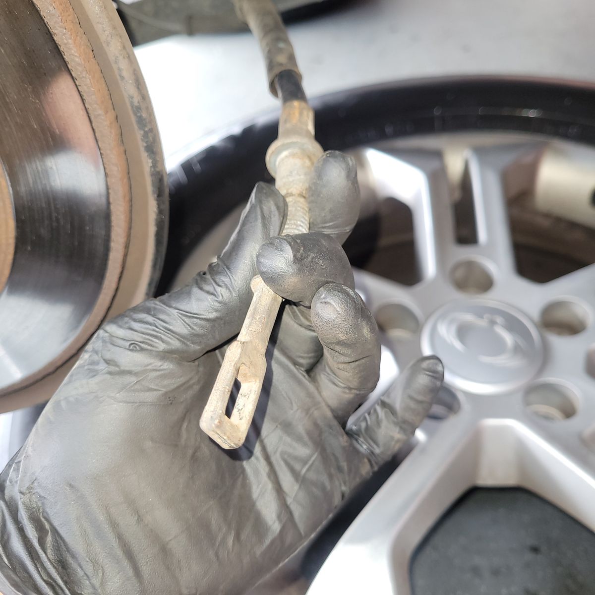 Close-up of a Parking Brake Cable on a Car Gloved hand holding a worn parking brake cable near car wheel hub.