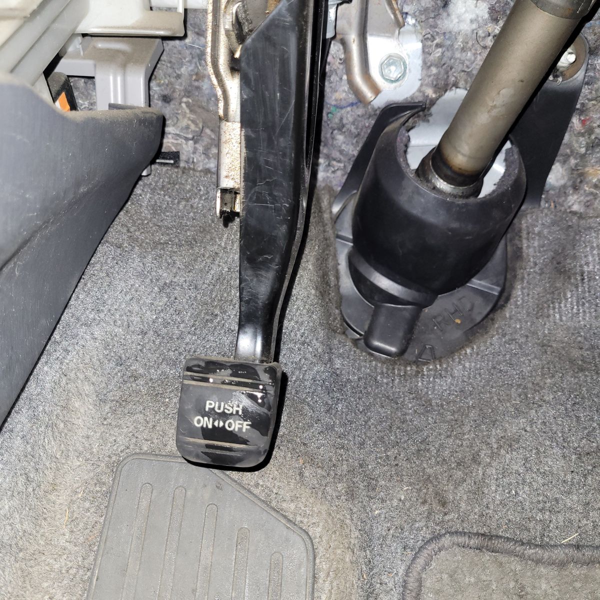 Close-up view of a car's parking brake pedal labeled 'PUSH ON/OFF.'