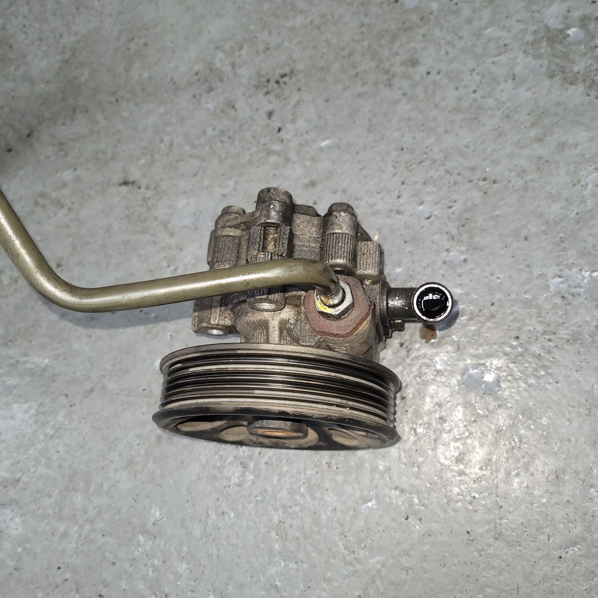 Used Power Steering Pump on Workshop Floor Disassembled power steering pump with pulley and metal tubing on concrete floor