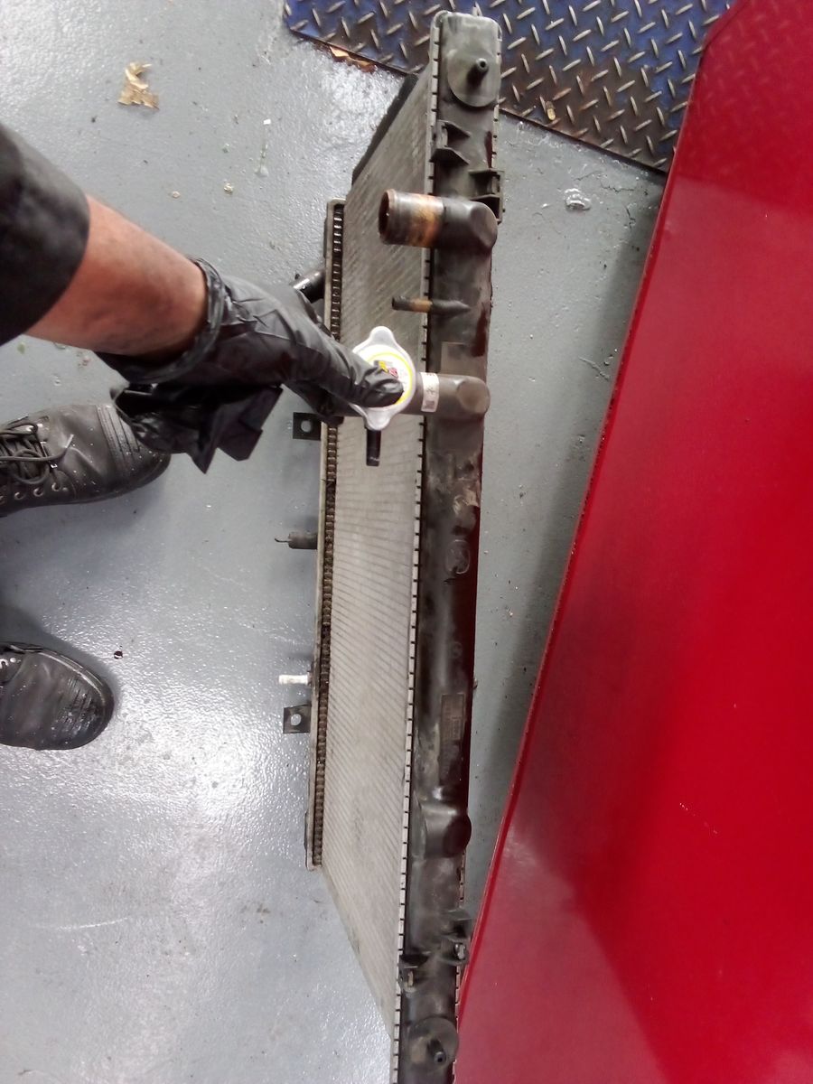 Gloved hand holds the cap of an upright car radiator in a garage.