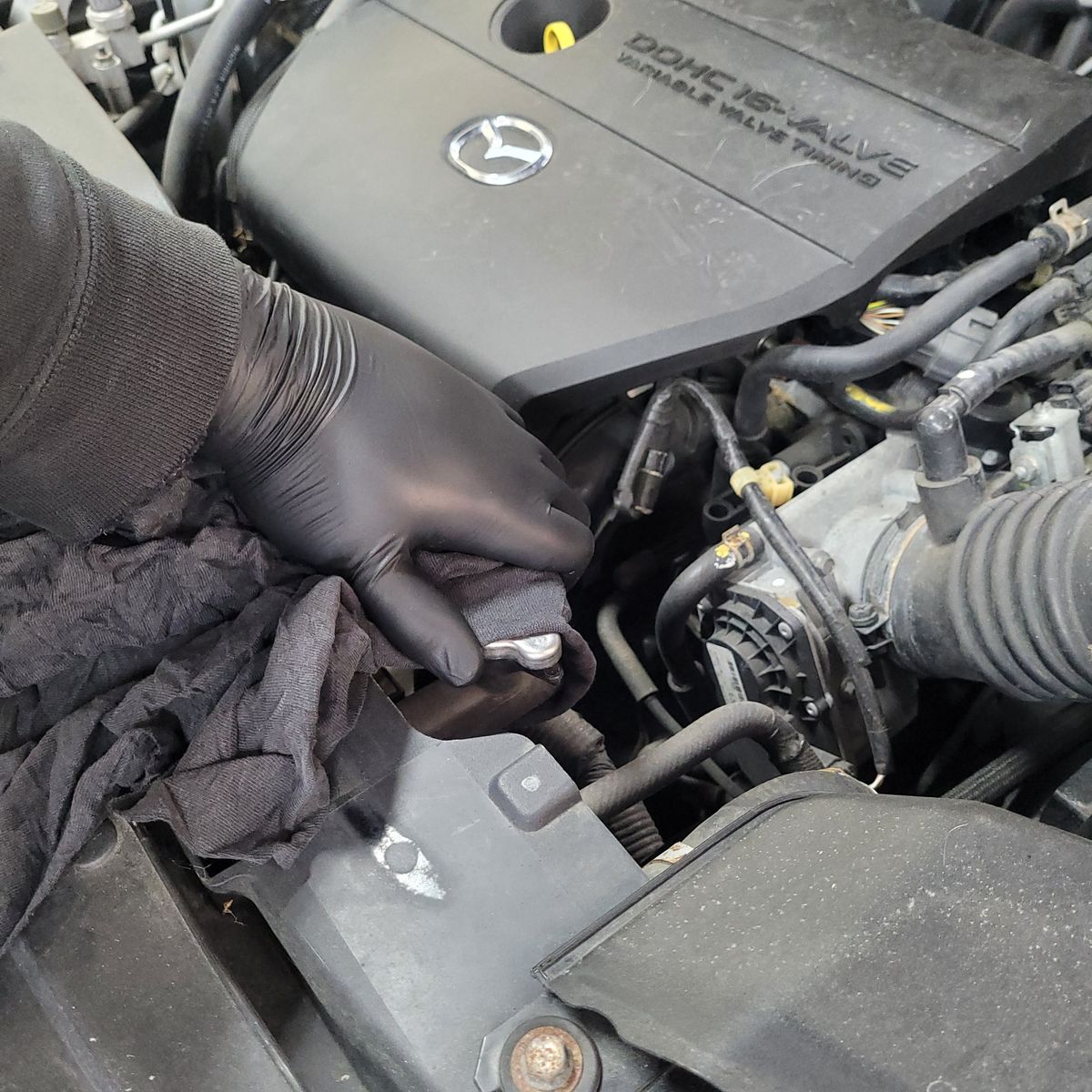 Removing Radiator Cap on Mazda Engine Gloved hand removing a radiator cap from a Mazda engine bay