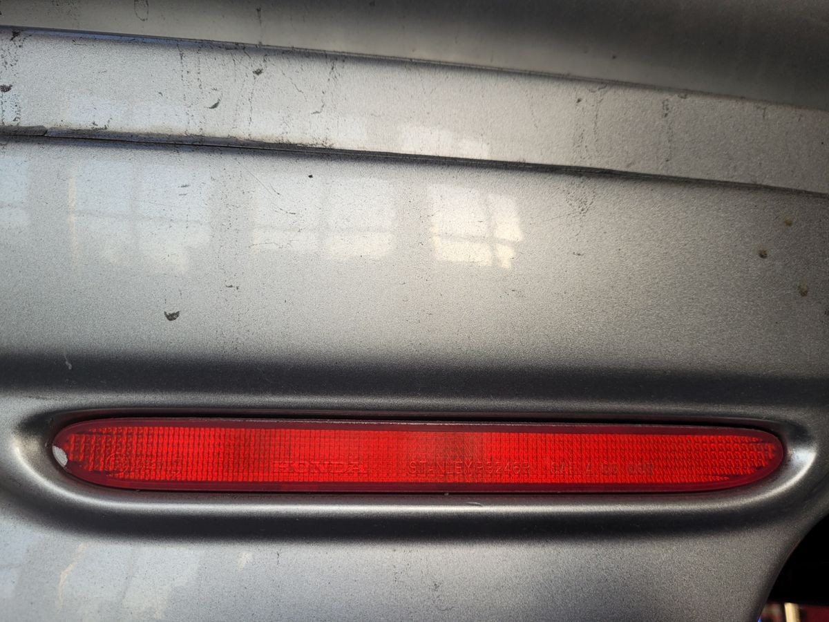 Red Reflector on Silver Car Bumper Close-up of a red reflector on a dusty silver car bumper.