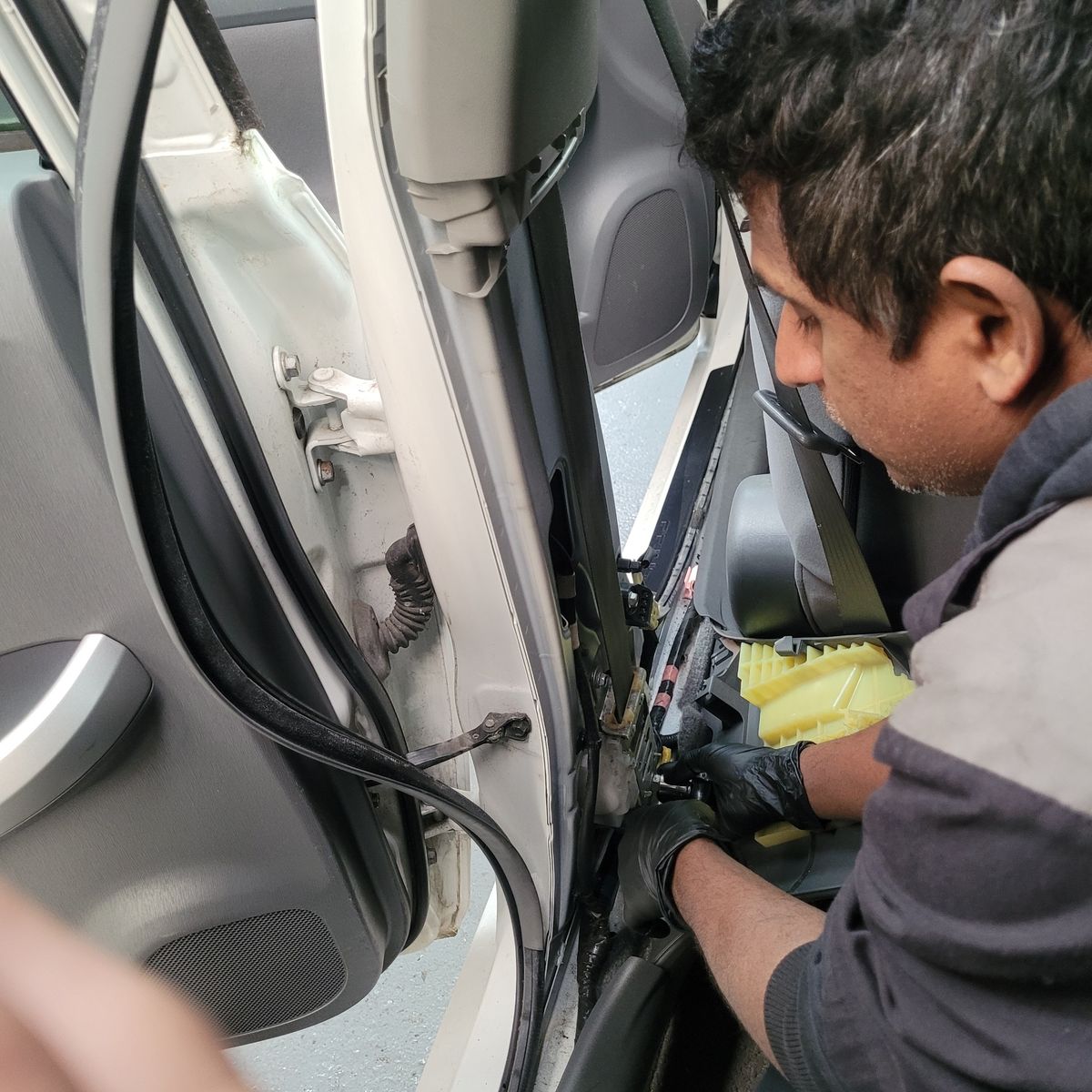 Mechanic carefully detaching seat belt assembly from car's interior frame.