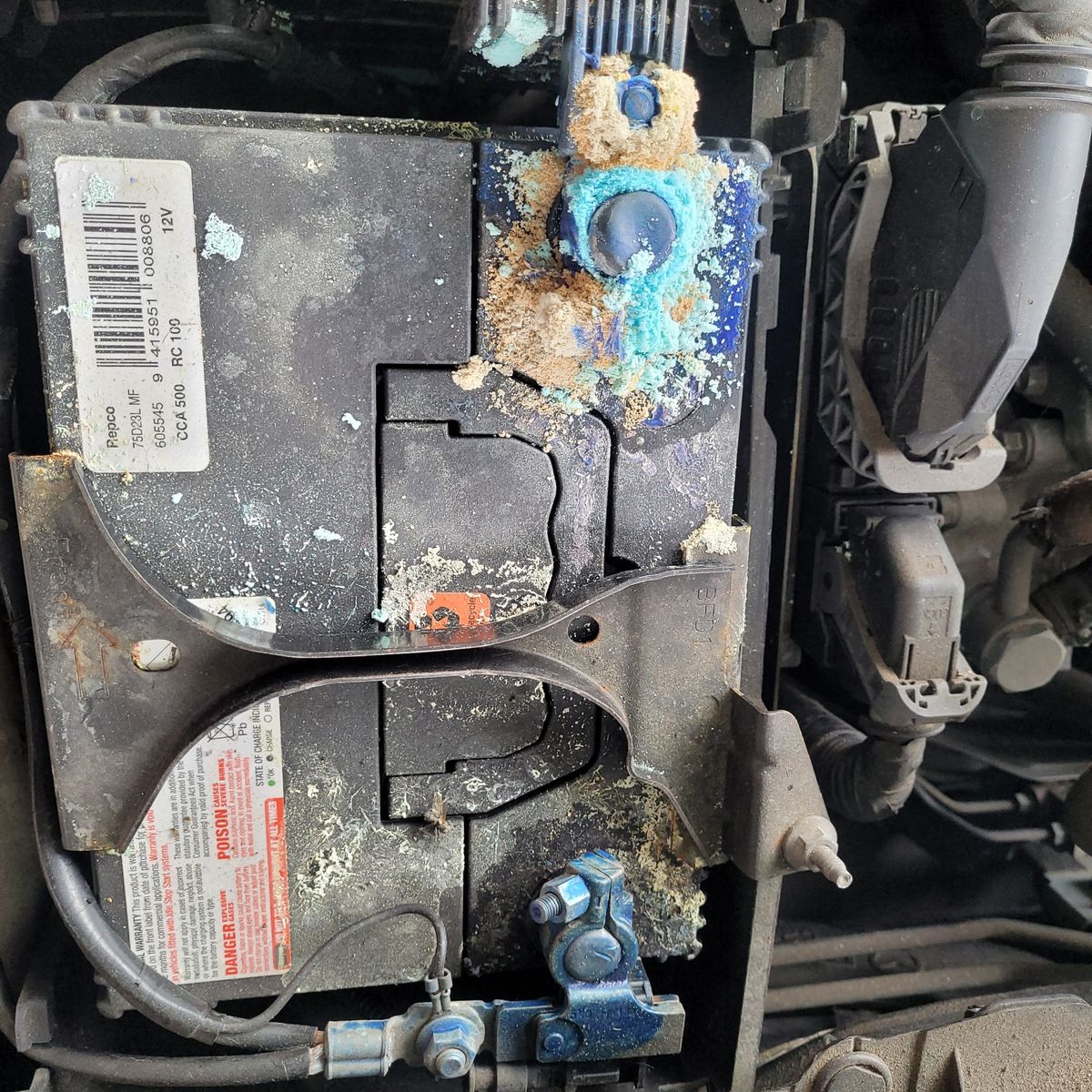 Close-up of a car battery with blue corrosion on the terminal.