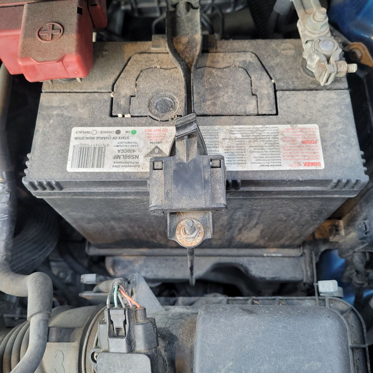 Car Engine Compartment Showing a 12V Battery Close-up of a dusty 12V car battery secured in the engine bay