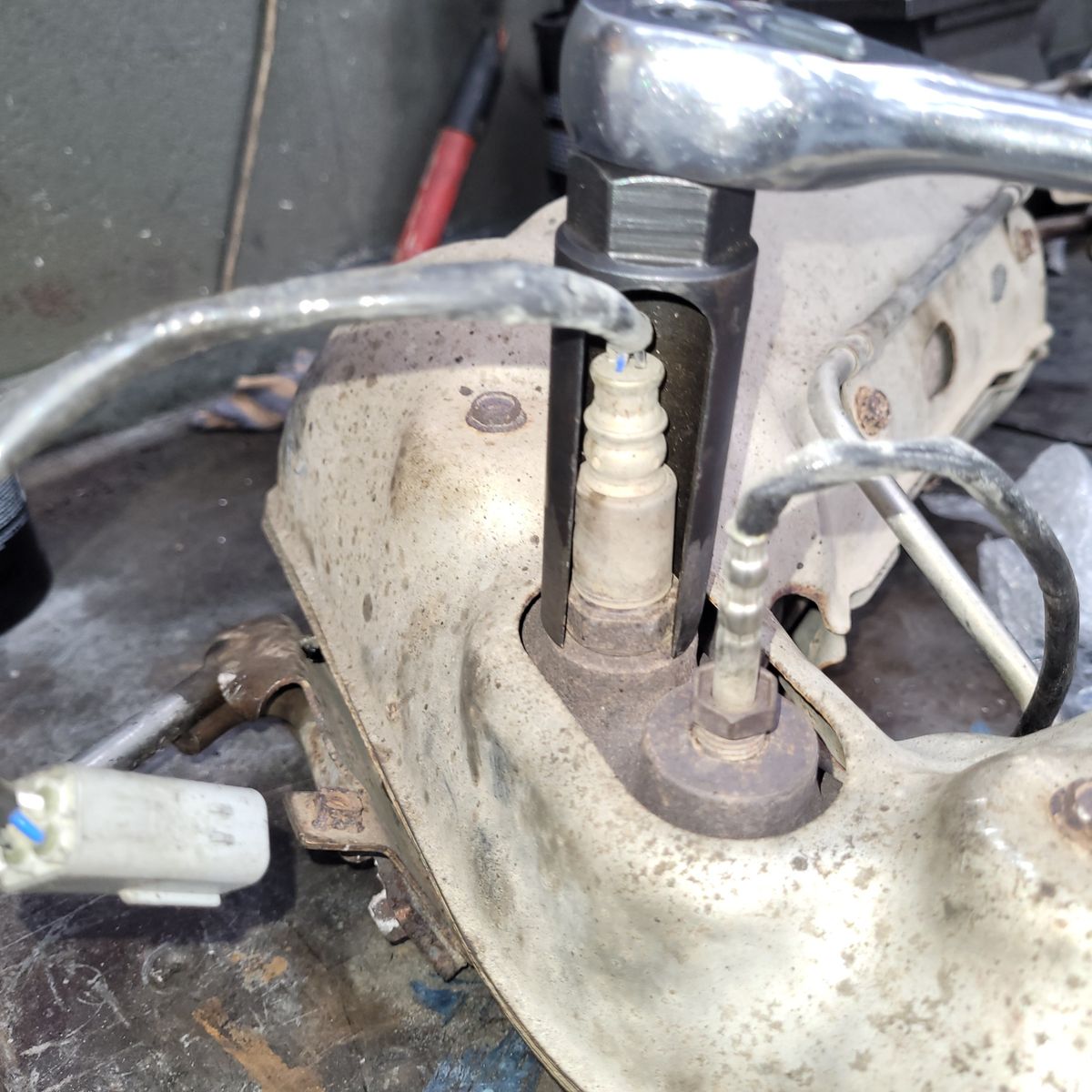Oxygen sensor being removed from a car exhaust manifold with a socket wrench.