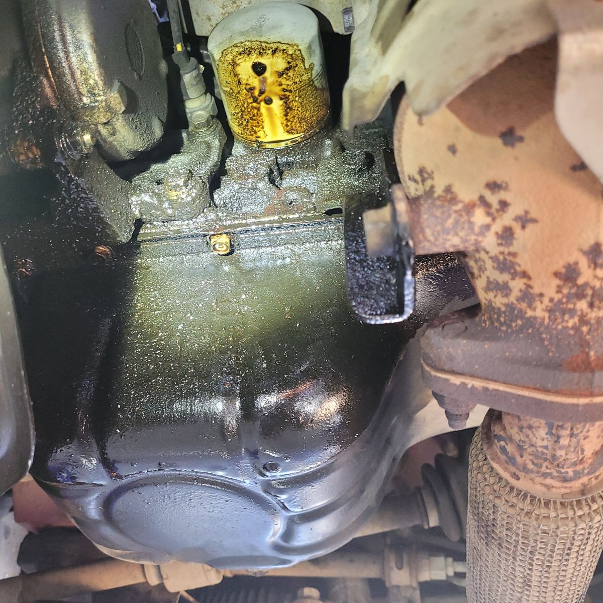 Engine Oil Sump Gasket Leak Close-Up Underside of a car engine showing oil sump and visible oil leaks
