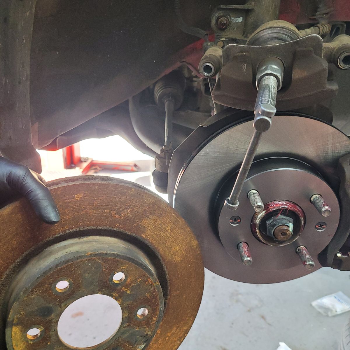 Old rusty brake rotor held near newly installed clean rotor on car