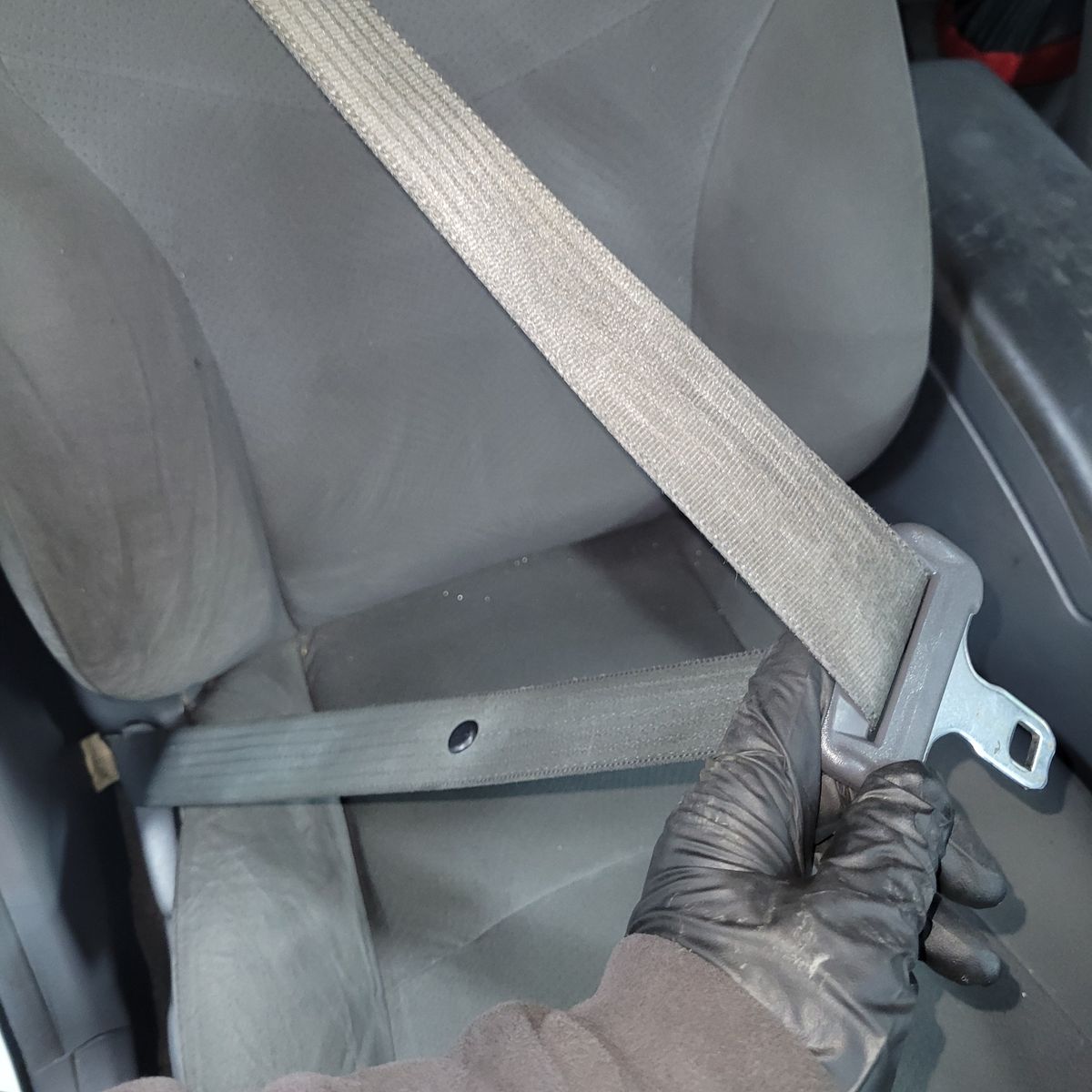 Car Seat Belt Replacement Process Gloved hand holding seat belt buckle on a car seat.