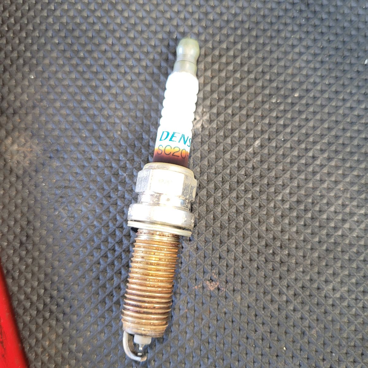 Used Spark Plug on Textured Mat Close-up of a single used spark plug on a black rubber mat.