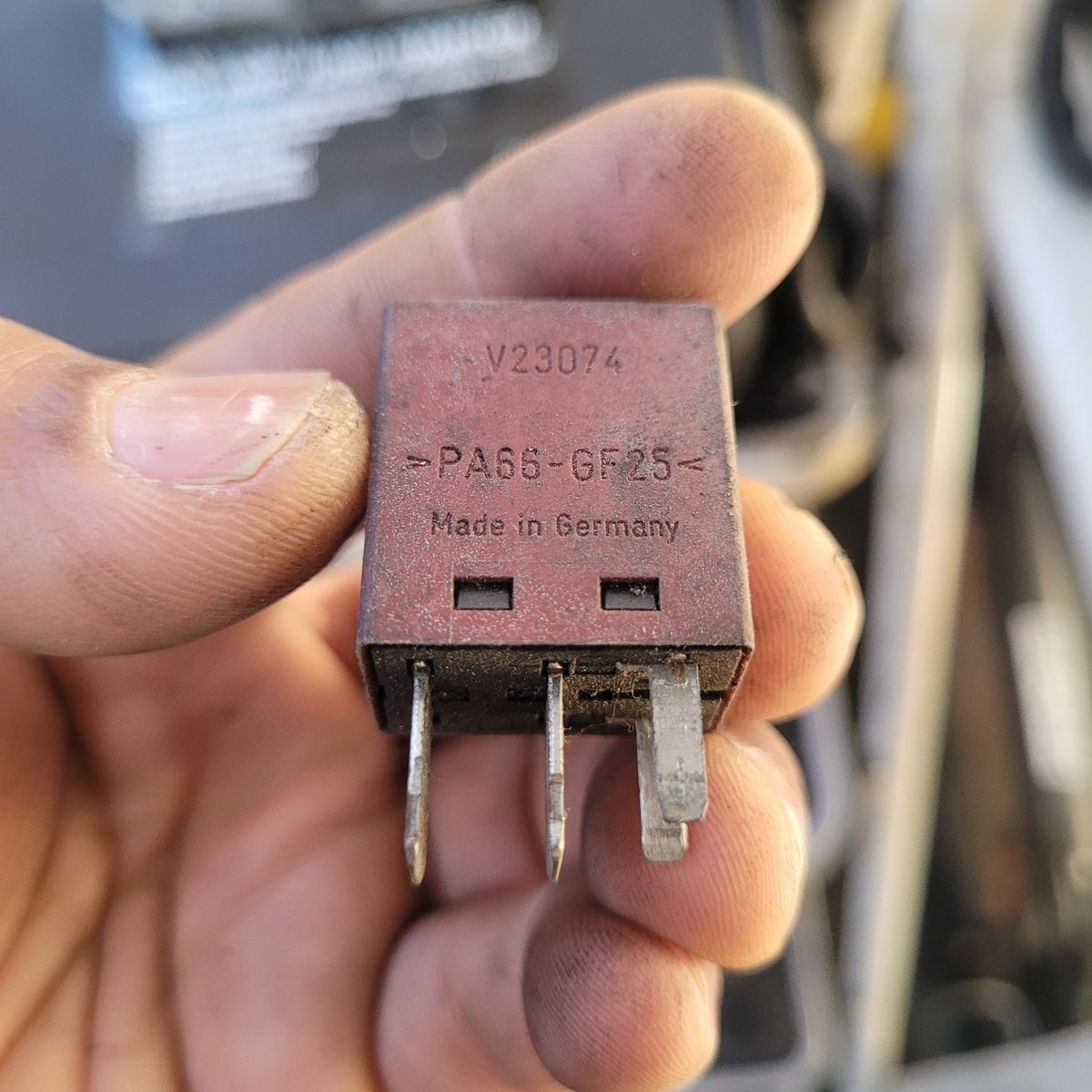 Close-up of Used Starter Relay Person holding a worn, German-made starter relay with visible prongs.
