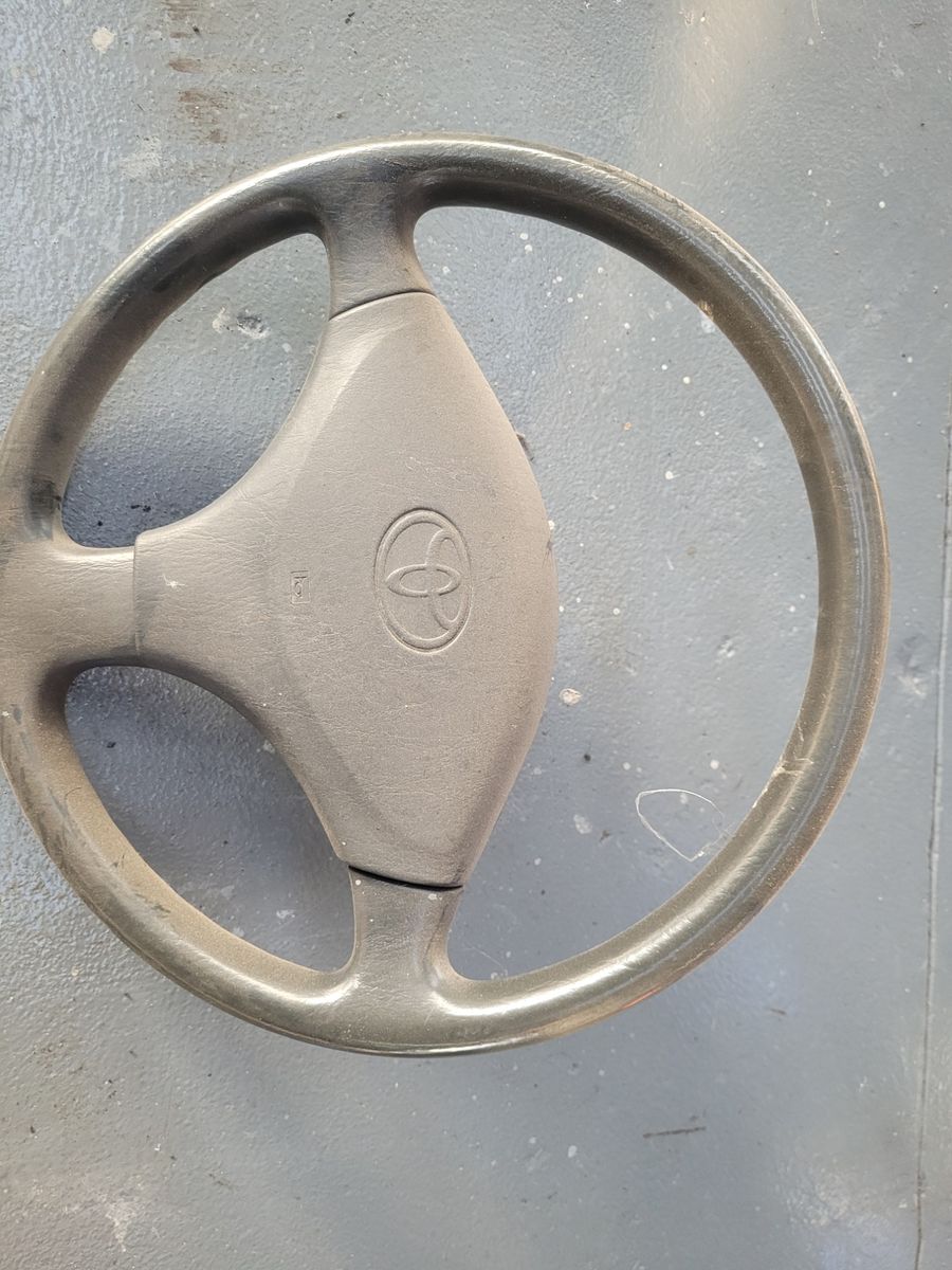 Old Toyota Steering Wheel on Concrete Floor Worn Toyota car steering wheel lying on a gray concrete surface.