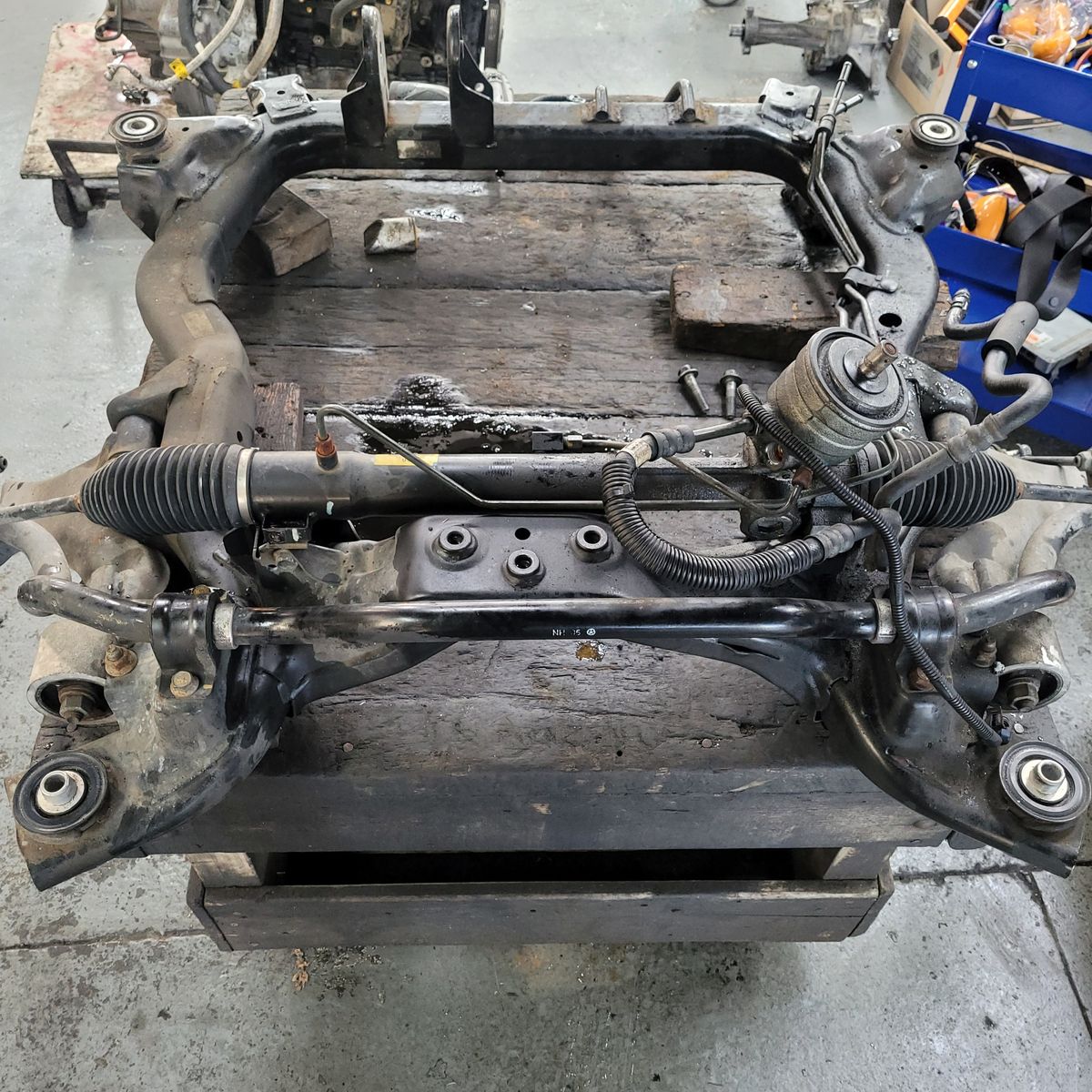 A metal automotive subframe with attached steering rack on a workshop bench