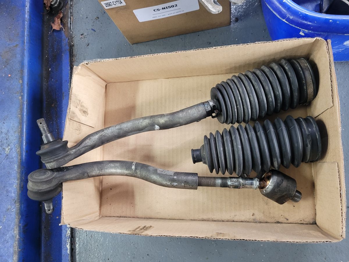 Used Suspension and Steering Components in Box Two worn suspension parts with rubber boots placed in a cardboard box.