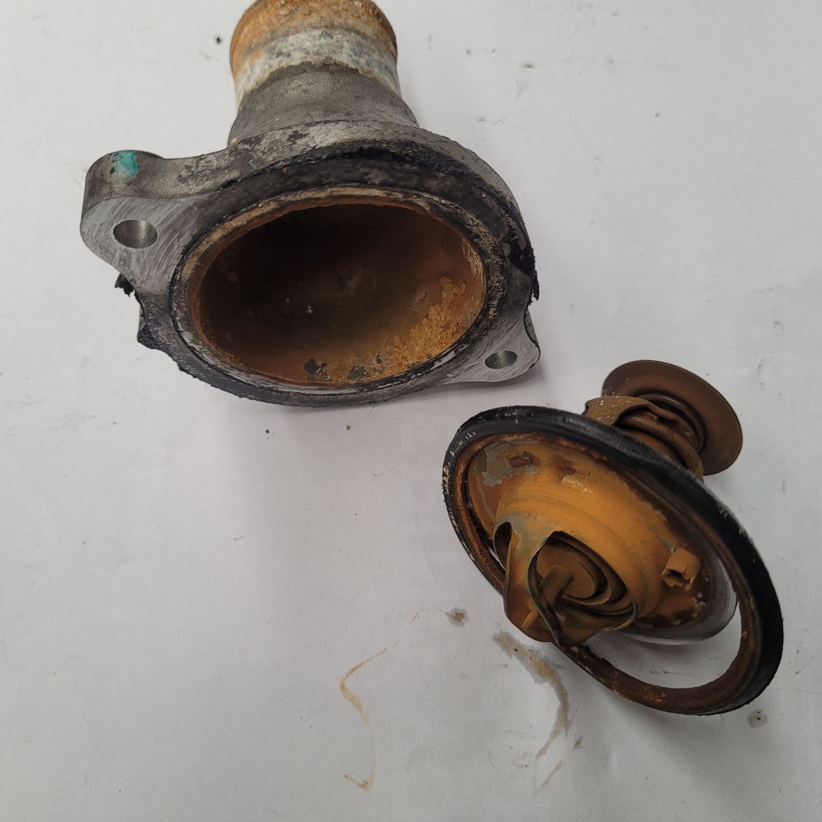 Corroded car thermostat housing and valve close-up Rusty, old automotive thermostat and housing on a white surface