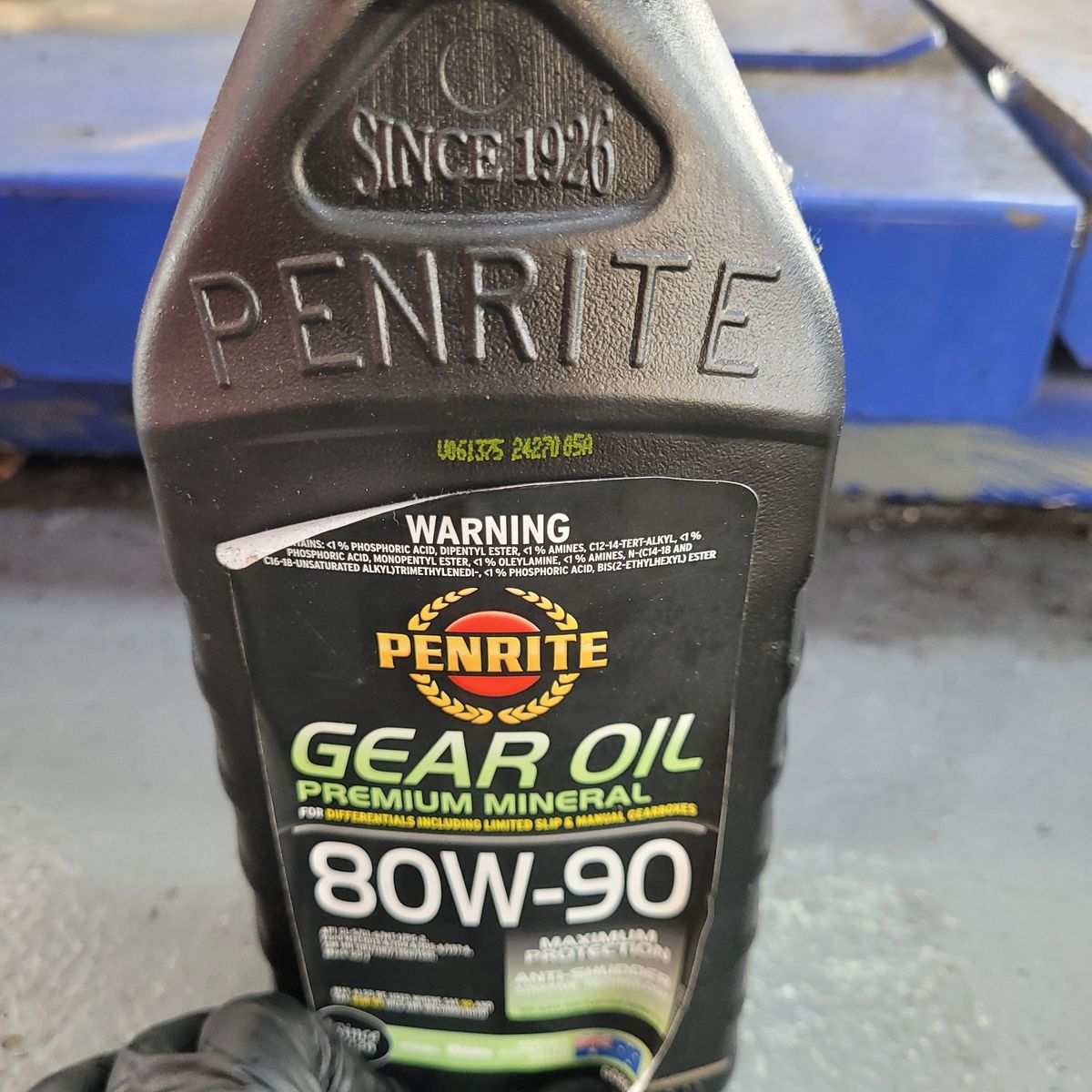 Penrite Gear Oil 80W-90 Bottle Close-Up Hand holding Penrite Gear Oil 80W-90 bottle on workshop floor.