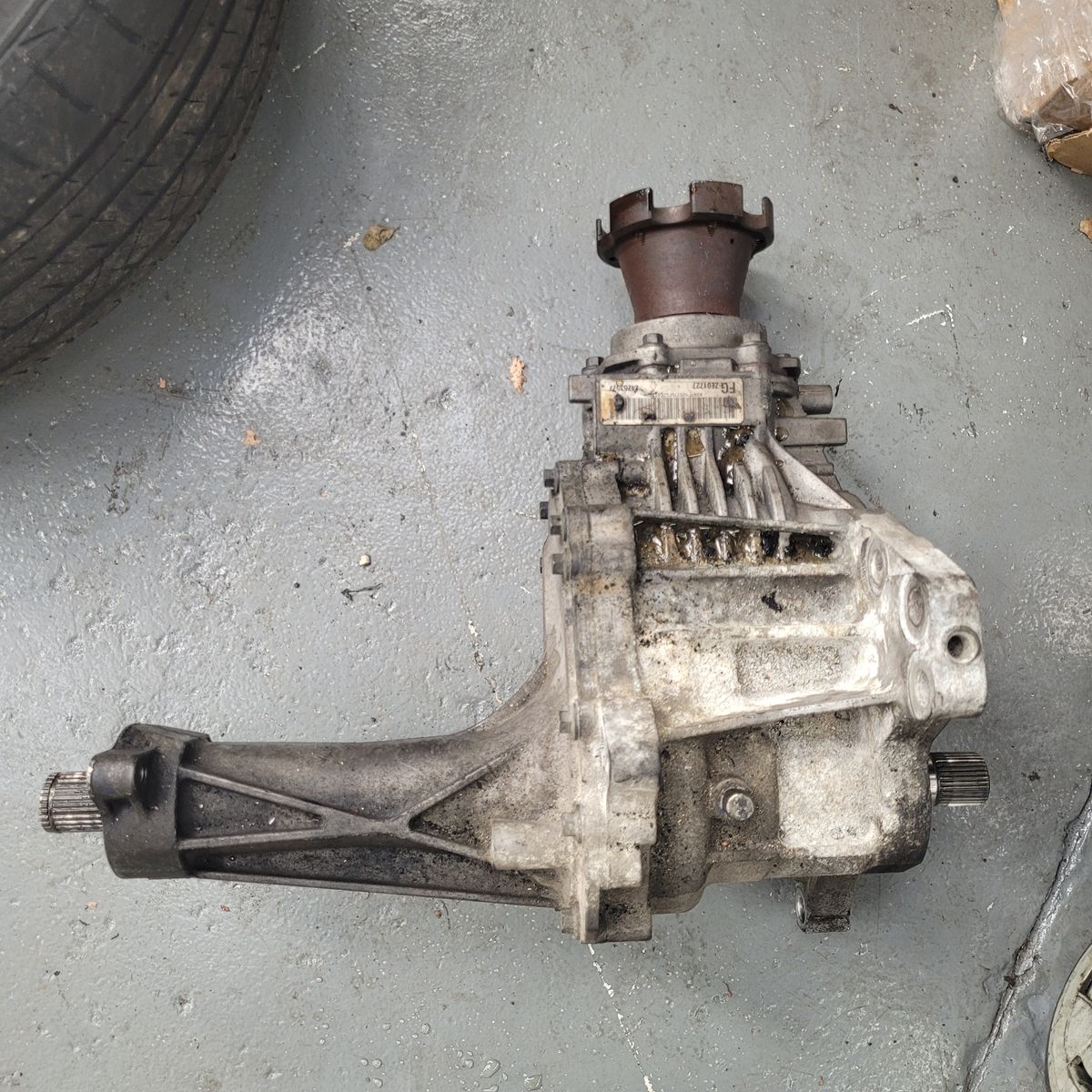 Used Vehicle Transfer Case on Workshop Floor A transfer case for a vehicle lying on a concrete garage floor