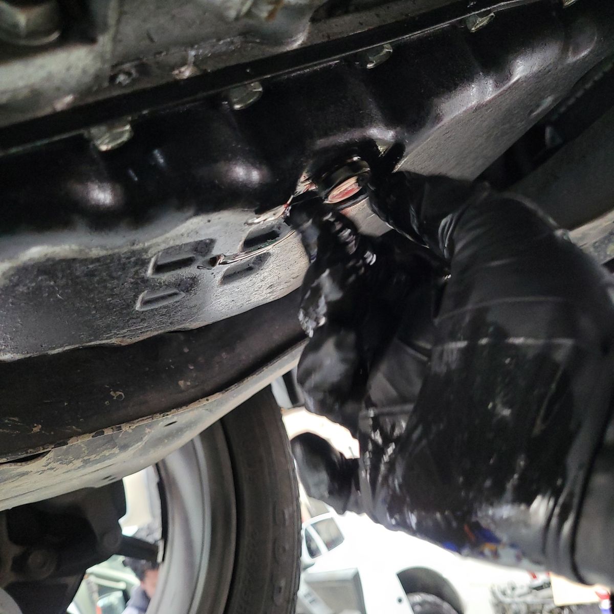 Transmission Oil Inspection Under Vehicle Mechanic's gloved hand checking transmission oil drain plug underneath a car