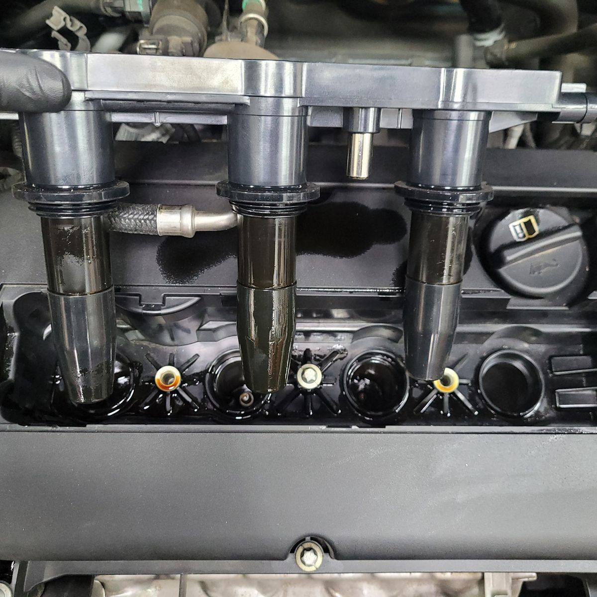 Close-Up of Valve Cover Gasket Area on Engine Exposed valve cover gasket with ignition coils and oil residue on a car engine