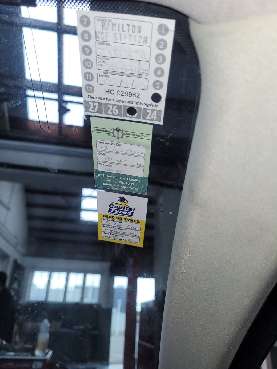 Warrant of Fitness, service, and tyre alignment stickers displayed on a vehicle windscreen.