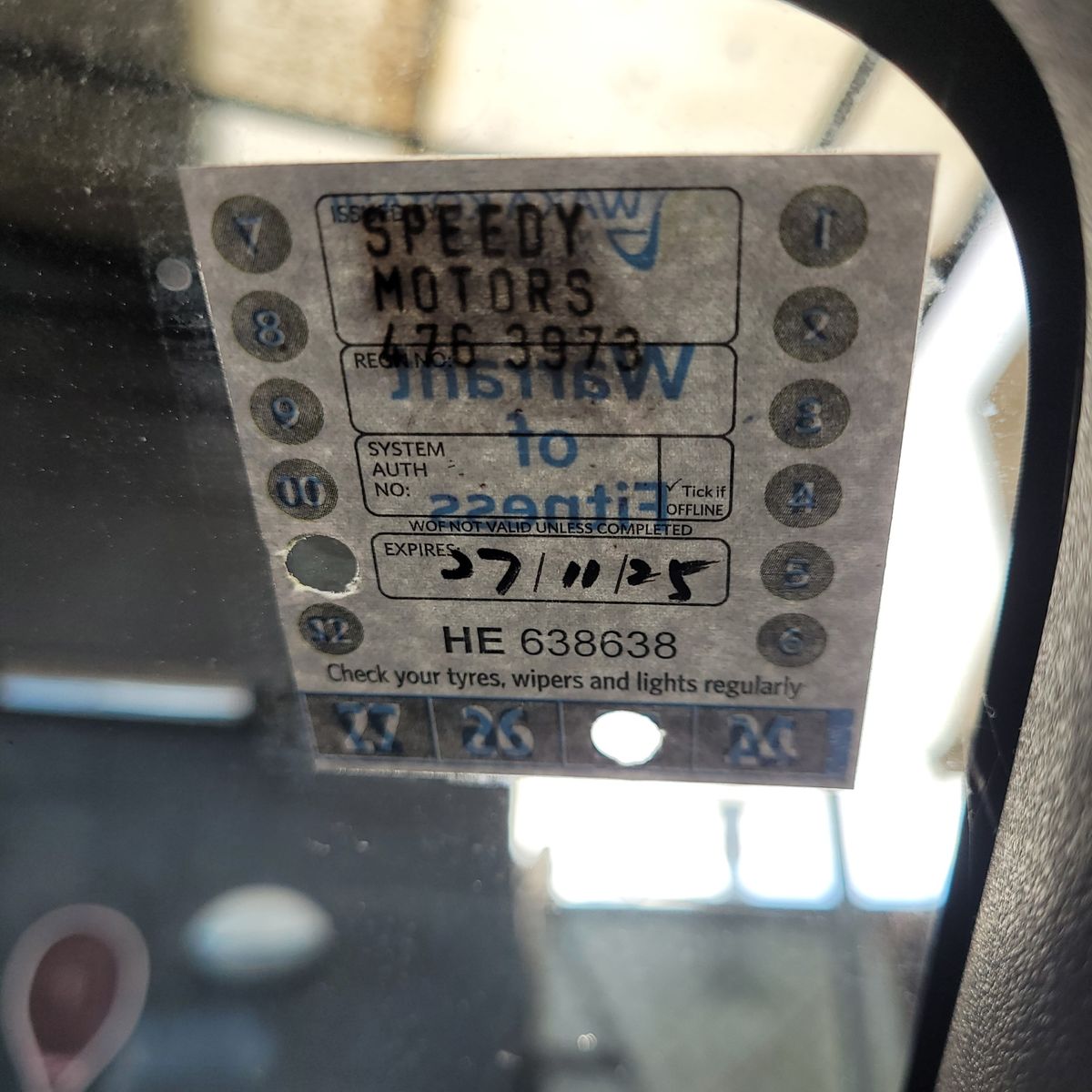 Warrant of Fitness Sticker on Car Windshield Close-up of a Warrant of Fitness (WOF) sticker showing expiration date on a car window.