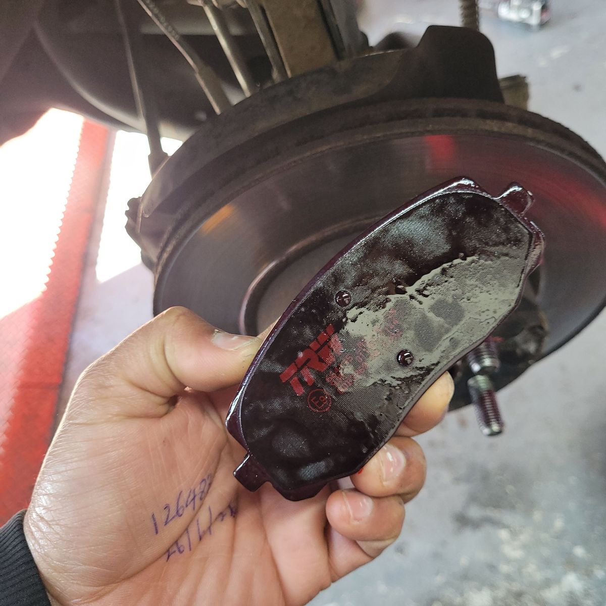Mechanic Holding New Brake Pad by Car Rotor Hand holding a new brake pad near a car brake rotor during installation