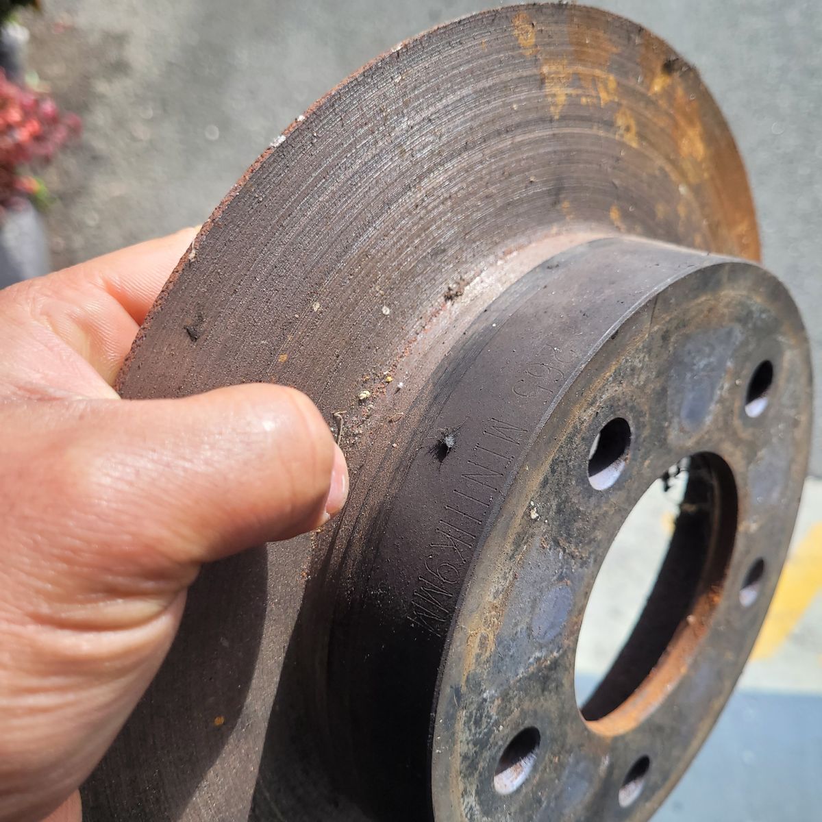 Worn Brake Rotor with Surface Scoring Hand holding a rusty, scored brake disc removed from a vehicle.
