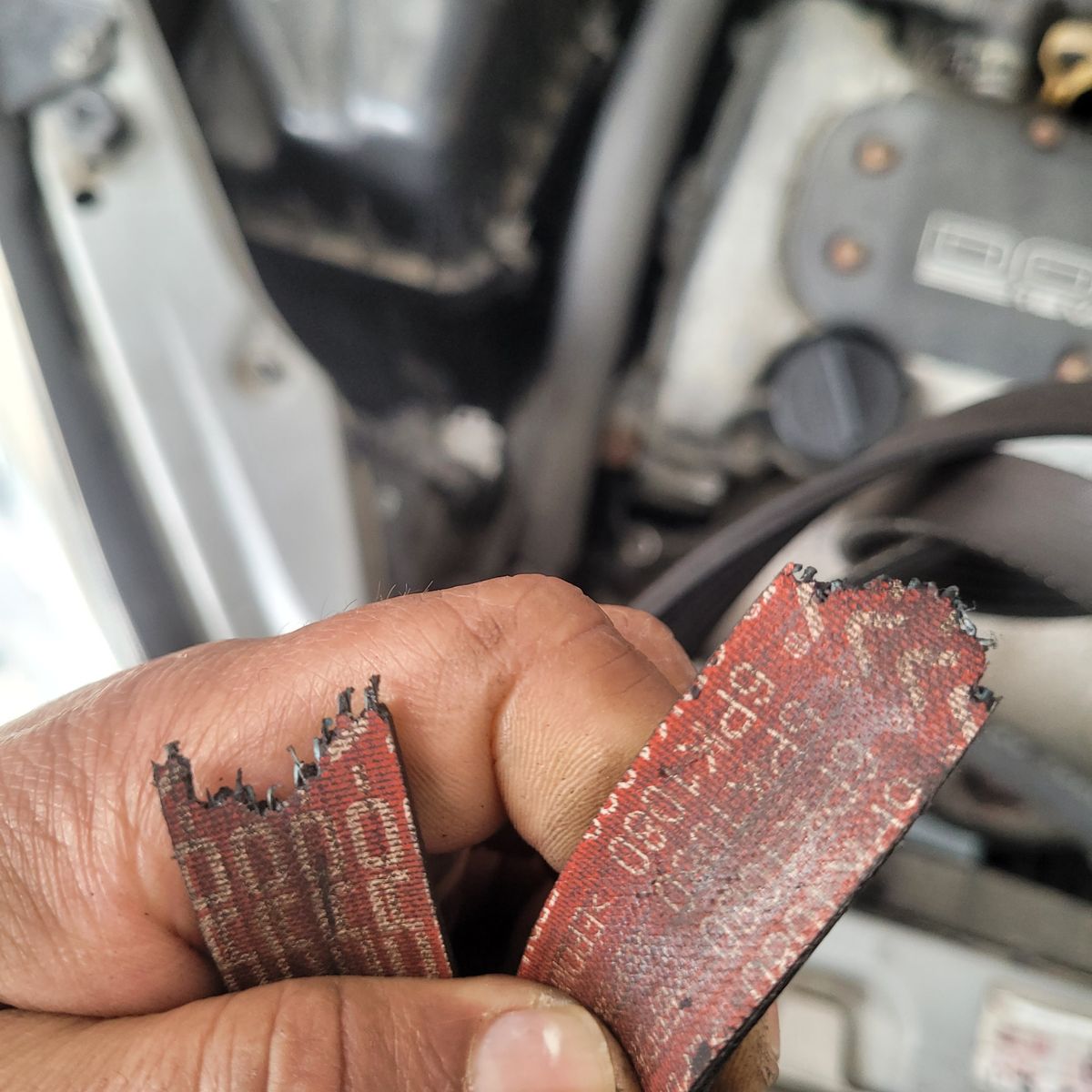 Mechanic holding a frayed, burnt car belt beside engine