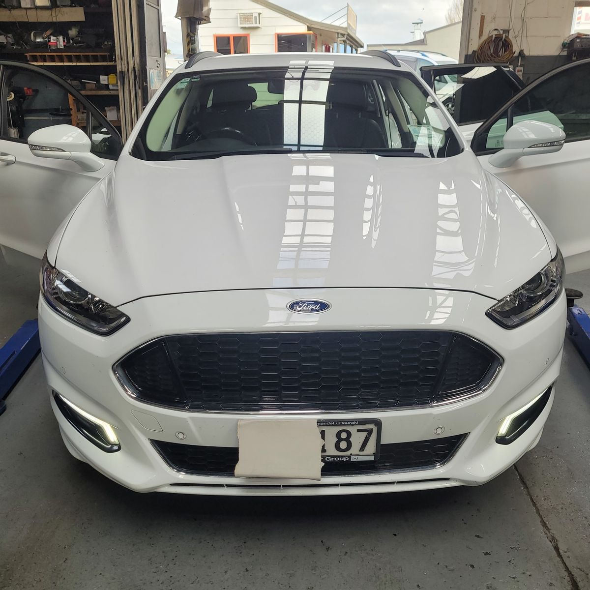 Front view of a white Ford sedan with doors open in a garage setting.
